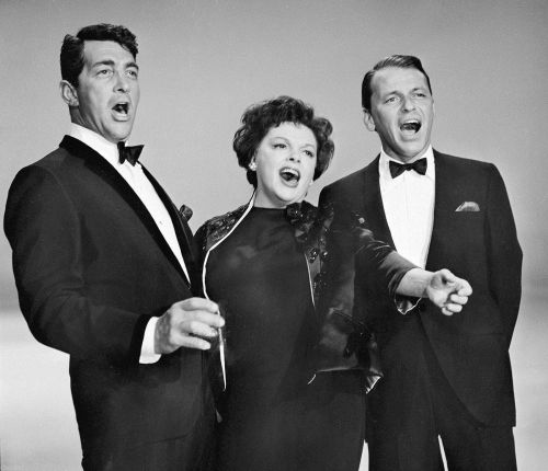 Three singers in formal attire perform together, expressing joy and energy on stage. Black and white photo.