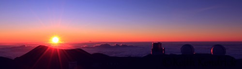 Sunrise over a mountain landscape, with observatory domes silhouetted against a colorful sky.