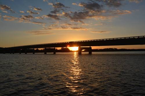 Silhouette of a bridge over water at sunset, with vibrant colors reflecting on the surface.