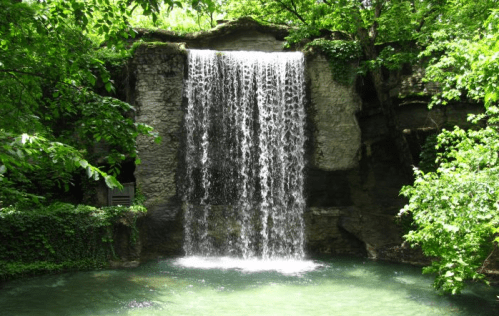 A serene waterfall cascading over rocks, surrounded by lush green trees and a tranquil pool below.