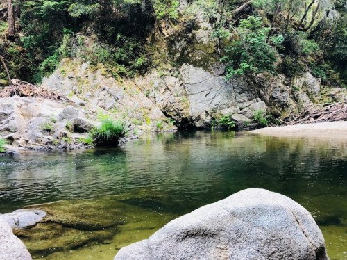 A serene river scene with clear water, surrounded by rocky banks and lush greenery.