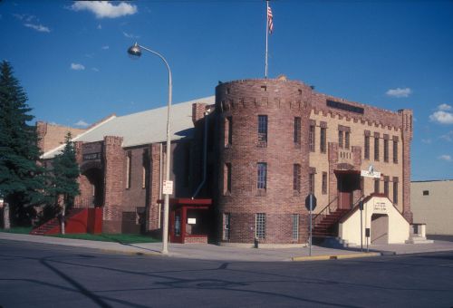 Historic brick building with a castle-like design, featuring a flag and surrounded by trees and a clear blue sky.