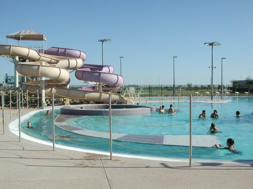 A water park featuring colorful slides, a pool with swimmers, and clear blue skies in the background.