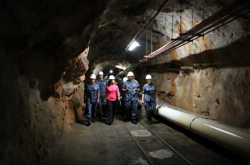 A group of people in hard hats walking through a dimly lit tunnel with rocky walls and pipes.