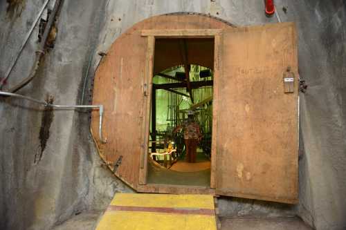 A large wooden door opens into a tunnel, revealing a dimly lit interior with industrial equipment and a circular design.