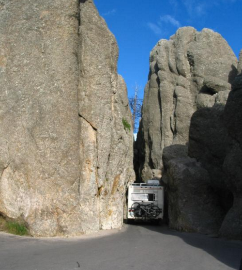 A narrow road between towering rock formations with a vehicle navigating through the tight space.