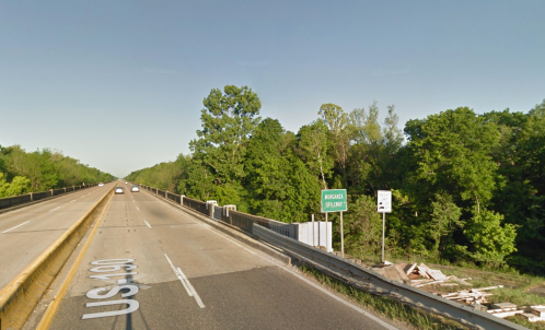 A wide highway with a green sign indicating "Burgan Plant," surrounded by trees and clear blue sky.