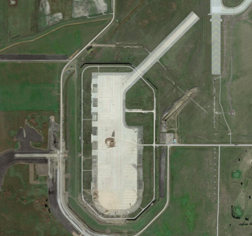Aerial view of a large, empty construction site with a runway and surrounding green fields.