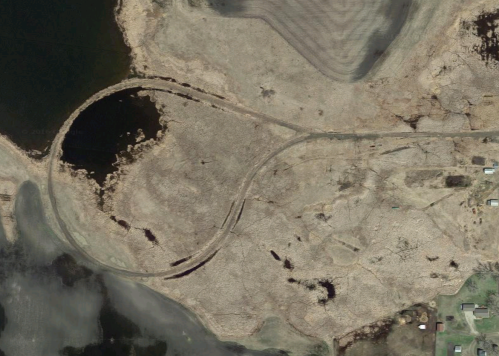 Aerial view of a winding road on a barren landscape near a body of water, with patches of land and vegetation visible.