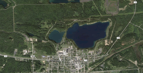 Aerial view of a small town surrounded by lakes and dense greenery, with roads and buildings visible.