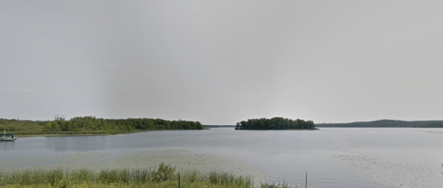 A serene lake view with an island in the distance, surrounded by lush greenery and calm waters.