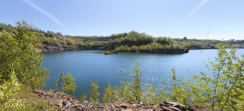 A serene lake surrounded by lush greenery and rocky cliffs under a clear blue sky.