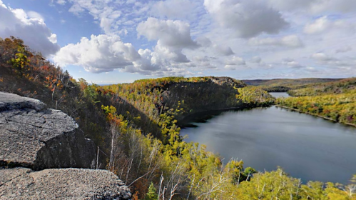 A scenic view of a river surrounded by lush greenery and rocky cliffs under a partly cloudy sky.