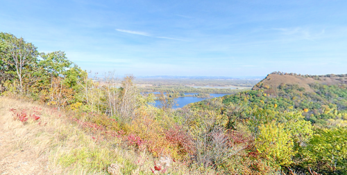 A scenic view of a river surrounded by colorful autumn foliage and rolling hills under a clear blue sky.