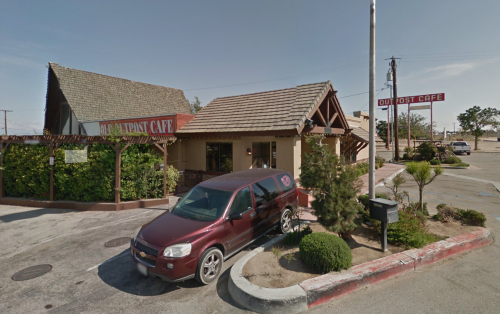 A rustic cafe with a sloped roof and a red SUV parked in front, surrounded by greenery and a clear blue sky.