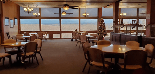 A spacious dining area with tables, chairs, and a Christmas tree, featuring large windows overlooking a scenic view.