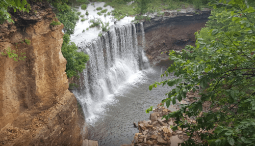 A serene waterfall cascading over rocky cliffs into a calm pool, surrounded by lush greenery.