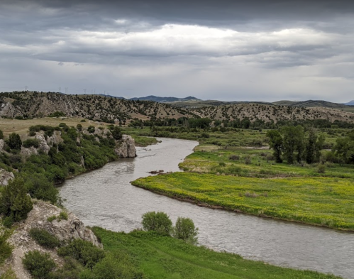 A winding river flows through green fields and rocky hills under a cloudy sky.