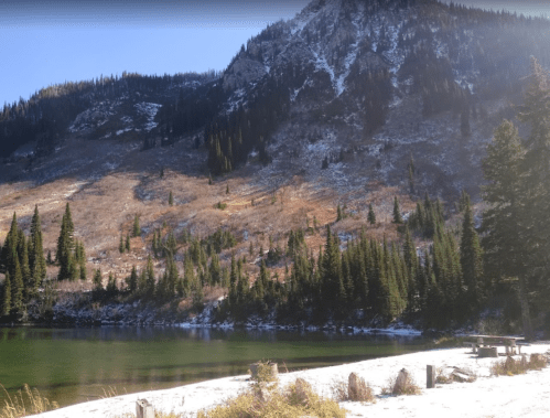 A serene lake surrounded by snow-dusted mountains and evergreen trees under a clear blue sky.