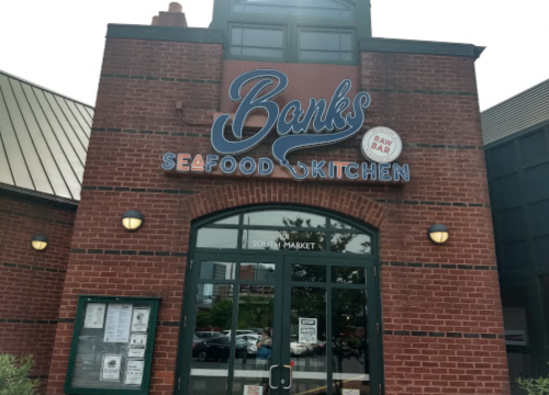 Exterior of Banks Seafood Kitchen, featuring a brick facade and a sign with the restaurant's name and a raw bar symbol.