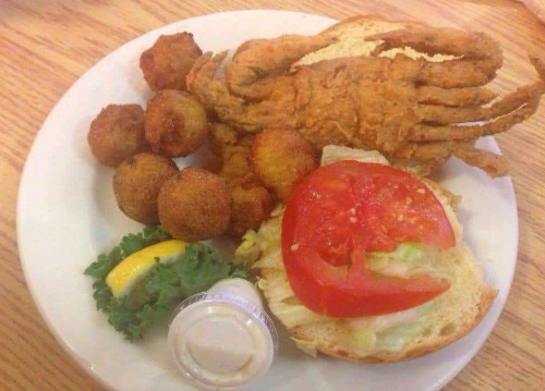 A plate of fried crab, hushpuppies, a sandwich with lettuce and tomato, and a lemon wedge.
