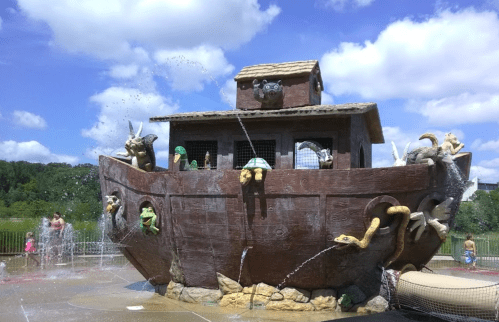 A large, whimsical boat structure with animal sculptures, surrounded by water features and a blue sky.