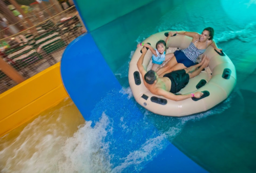 A family enjoys a water slide, riding a large inflatable tube down a colorful slide into a splash of water.