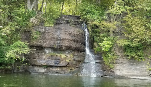 A serene waterfall cascading down rocky cliffs, surrounded by lush green trees and reflecting in calm water below.