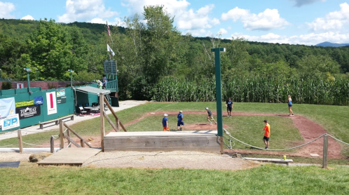 A baseball field with players practicing, surrounded by trees and a clear blue sky.