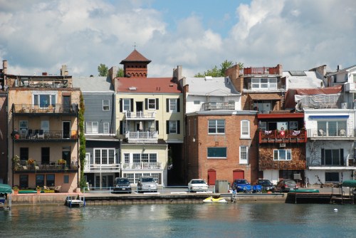 Colorful waterfront houses with balconies and a cloudy sky reflected in the water.