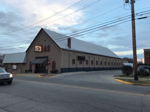 A large, brick building with a sloped roof, featuring a sign and striped awning, set against a cloudy sky.