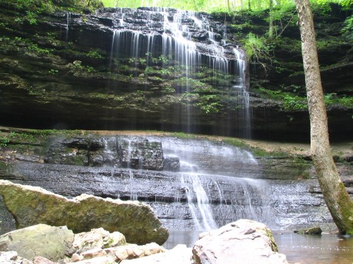 A serene waterfall cascading over rocky cliffs, surrounded by lush greenery and a tranquil pool below.