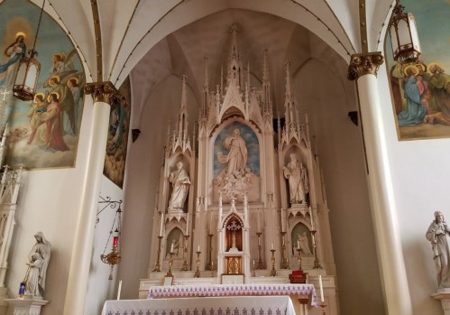 Interior of a church featuring an ornate altar with statues, paintings, and decorative arches.