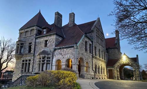 A historic stone mansion at dusk, featuring turrets and an archway, with a full moon visible in the sky.