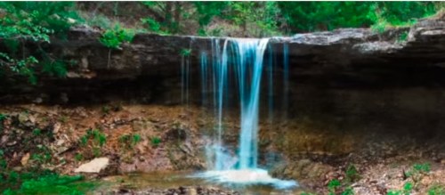 A serene waterfall cascading over rocky terrain, surrounded by lush greenery and a tranquil pool below.