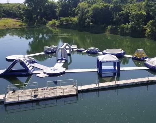 A floating water park with inflatable structures on a calm lake, surrounded by greenery and a wooden dock.