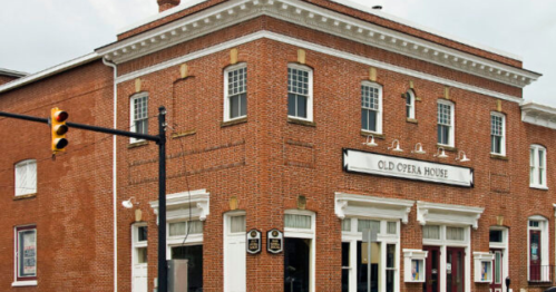 Historic brick building with a sign reading "Old Opera House" and large windows, located at a street intersection.
