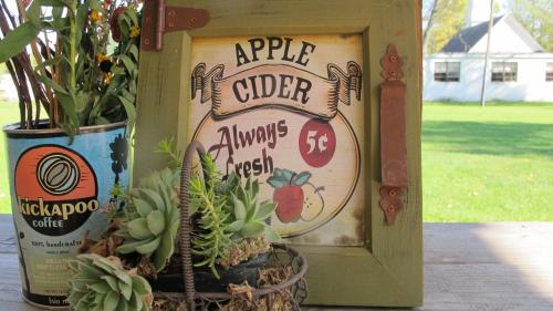 A rustic frame displays an "Apple Cider" sign, with a coffee can and a succulent planter in the foreground.