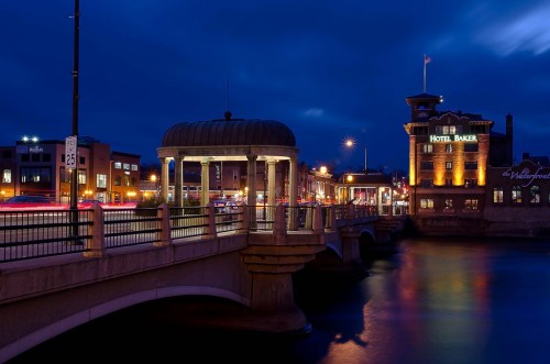 A scenic view of a bridge at night, with illuminated buildings and a river reflecting the lights.