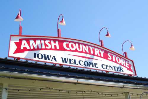 Sign for "Amish Country Store" and "Iowa Welcome Center" with bright blue sky in the background.