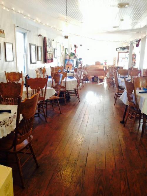 A cozy restaurant interior with wooden floors, tables set with white tablecloths, and rustic chairs.