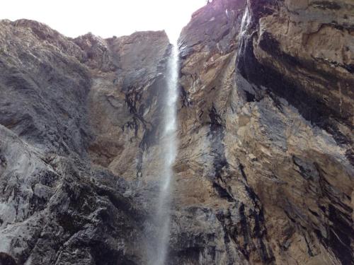 A tall waterfall cascades down rocky cliffs, surrounded by rugged stone formations and mist rising from the water.