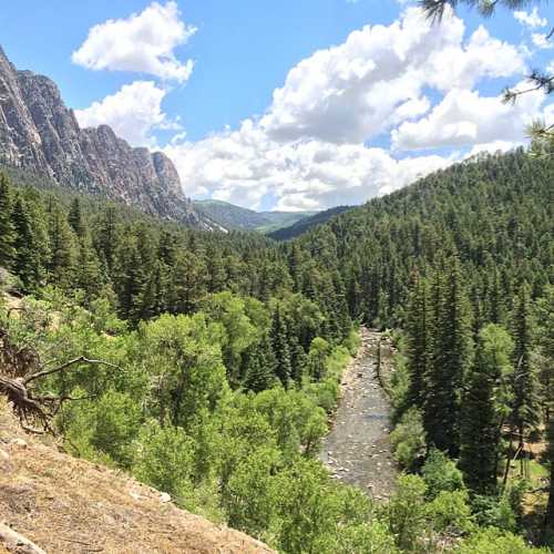 A scenic view of a lush green valley with a winding river, surrounded by mountains and a blue sky with fluffy clouds.