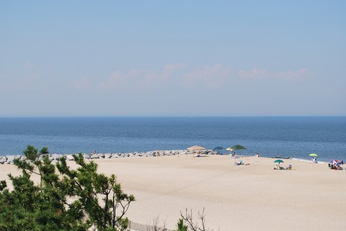 A serene beach scene with soft sand, umbrellas, and calm blue waters under a clear sky.