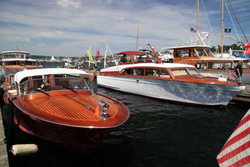 Two classic wooden boats docked at a marina, with colorful flags and people in the background enjoying the day.