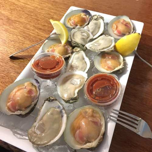 A platter of fresh oysters on ice, garnished with lemon wedges and served with dipping sauces.