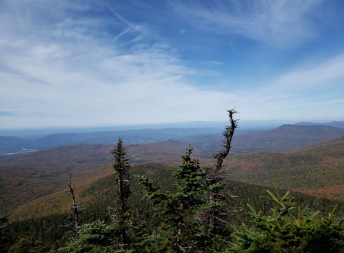 A panoramic view of mountains with autumn foliage under a blue sky with wispy clouds.