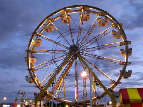 A brightly lit Ferris wheel against a twilight sky, with colorful lights illuminating the ride.