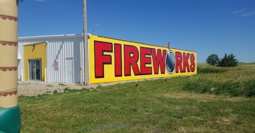 A large building with a bright yellow and red sign that reads "FIREWORKS" against a clear blue sky.
