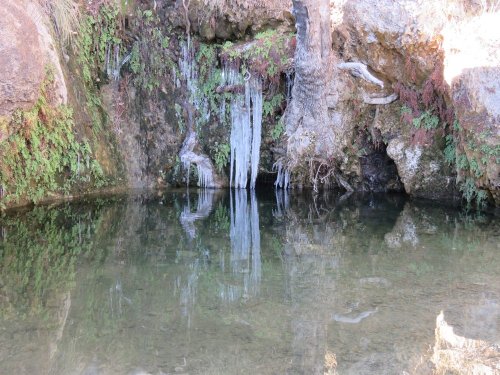 A serene natural pool surrounded by rocky terrain and lush greenery, reflecting the surrounding landscape.